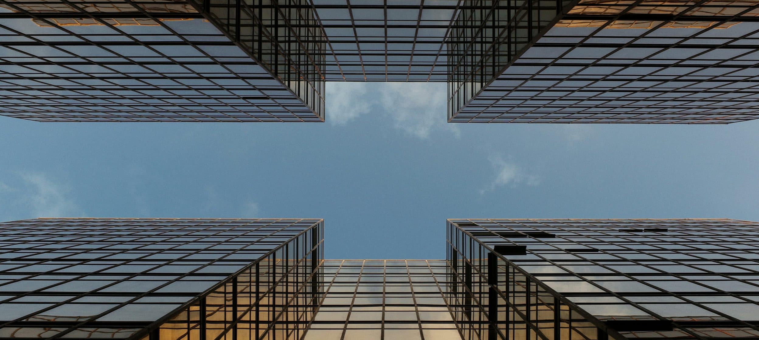Façades de verre de quatre immeubles vues d'en bas, ciel bleu au centre