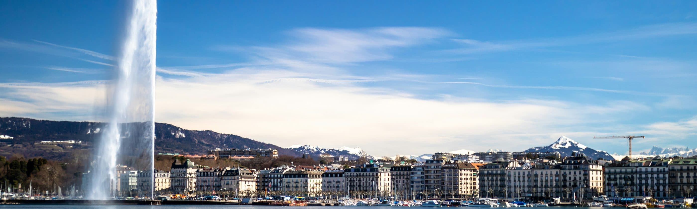 Un jet d'eau au bord du lac, la ville et les montagnes en arrière-plan